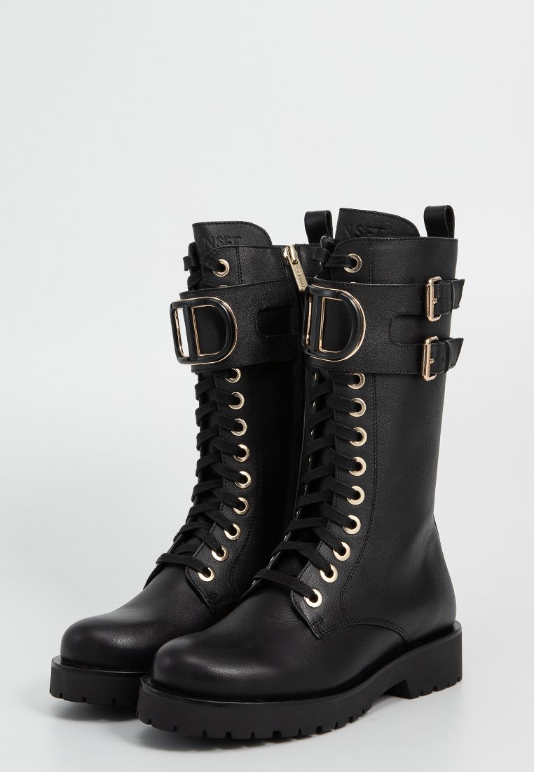 Bottes noires en cuir jusqu'au genou avec quincaillerie dorée, dotées d'un laçage à l'avant, de zippers latéraux et d'accents à double boucle. Semelle plate en caoutchouc.