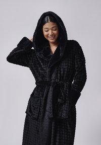 Sort hættebadekåbe lavet af blødt plysstof med et tekstureret ternet mønster, forlommer foran og bånd til at binde i taljen. Blød og varm udseende.