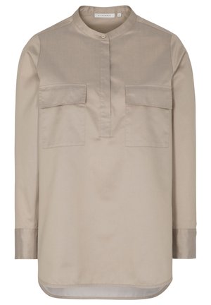 Chemise beige clair à manches longues avec col mao, deux poches avant à rabat, patte de boutonnage et ourlet arrondi.
