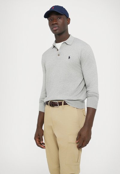 Világosszürke hosszú ujjú galléros póló három gombos patttal és sötétkék logóval, khaki színű cargo nadrággal és tengerészkék sapkával párosítva.