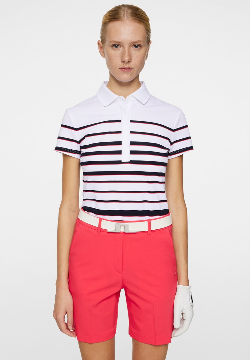 Krageskjorta i vitt med marinblå och röda ränder; kombinerad med klarröda shorts och ett vitt bälte. En handske synlig på höger sida.