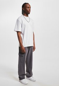 White short-sleeve t-shirt paired with gray cargo pants featuring side pockets, complemented by white sneakers and a silver chain necklace.