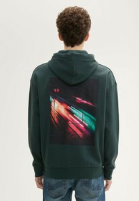 Ciemnozielona bluza z kapturem z dużym graficznym nadrukiem z tyłu, przedstawiającym żywe kolorowe smugi, symbolizujące ruch. Miękka tekstura materiału.