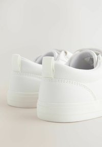 Hvide sneakers i et glat læderlignende materiale, lavt design, rund tå og flad gummisål. Har diskrete syninger og trækflapper.