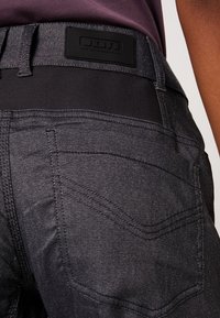 Harmaat farkut, joissa musta joustava vyötärönauha, koristeompeleet takataskuissa ja brändilogo vyötärönauhan yläpuolella.