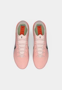 Sportowe buty Nike w miękkiej różowej siateczce, zwężanym kształcie, z czarnym logo, białymi sznurowadłami i kontrastującą niebieską podeszwą. Ukryty system sznurowania.