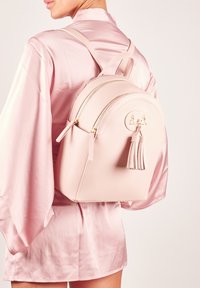 Zaino in ecopelle rosa con forma arrotondata, doppie cerniere e un tassello decorativo. Cuciture sottili e dettagli in oro.