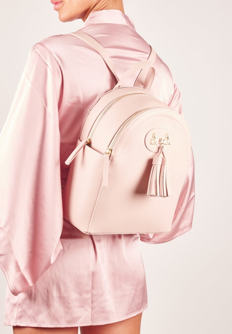 Zaino in ecopelle rosa con forma arrotondata, doppie cerniere e un tassello decorativo. Cuciture sottili e dettagli in oro.