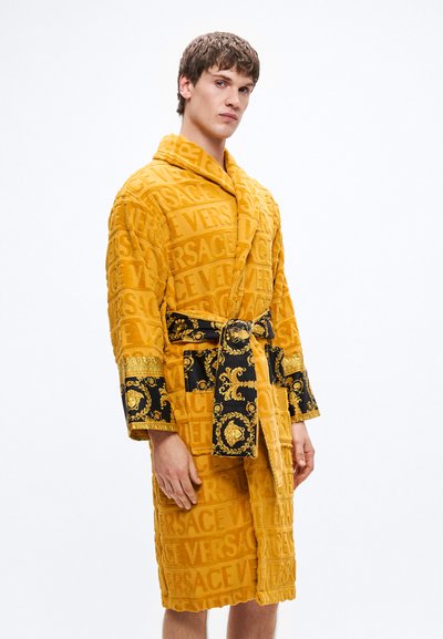 Rumeno frotirasto kopalni plašč z izrezljanim logotipom "VERSACE", črnim okrašenim pasom in manšetami, z zlato baročnimi vzorci za kontrast.