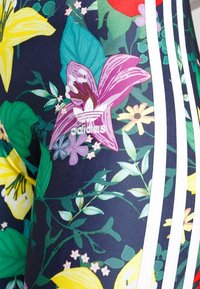 Blommiga leggingar med en marinblå bas prydd med livliga gula, rosa och gröna mönster, kompletterade med vita ränder och en Adidas-logotyp.