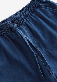 Navy blue cotton shorts with an elastic waistband, drawstring, and subtle textured fabric. Features horizontal ribbing and reinforced stitching.