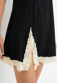 Camicia da notte nera con orlo scallop, dotata di pizzo avorio e dettagli a spacco sui lati, realizzata in tessuto morbido e leggero.