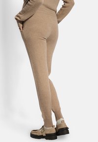 Pantalones de punto beige con un ajuste ceñido, que cuentan con una cintura elástica alta y bolsillos laterales, combinados con zapatos ligeros y texturizados.