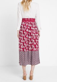 Rød og hvid blomsteret mønster nederdel med smocket talje. Den nederste del har geometrisk print. Længde til midt på læggen, letvægtsstof.