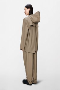 Világosbézs vízálló dzseki kapucnival és laza szabással, hozzáillő világosbézs nadrággal párosítva. Az anyag sima tapintású és elasztikus mandzsettákkal rendelkezik.