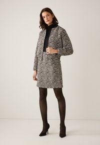 Schwarz-weißer Leopardenmuster-Jacken- und Rock-Set, kombiniert mit einem eng anliegenden schwarzen Rollkragenpullover und gemusterten schwarzen Strumpfhosen, vervollständigt mit schwarzen Absätzen.