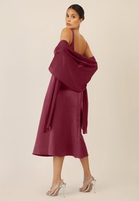 Burgundy satin dress with a flowing, layered shawl and sleek, strappy silver heels. Smooth texture with a fitted bodice and flared skirt.