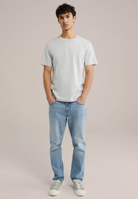 Šviesiai pilkas trumpas rankovėmis marškinėliai su apvalia iškirpte, derinami su šviesiai mėlynomis tiesiomis kelnėmis ir šviesiai žaliais sportbačiais. Paprasta, lygi tekstūra.