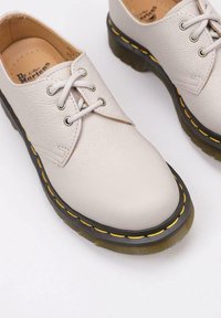 Scarpe in pelle grigia chiaro con lacci, punta arrotondata, suola nera spessa e cuciture gialle lungo il bordo. Design semplice e stile classico.