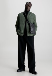 Giacca bomber verde, dolcevita nera, pantaloni larghi neri e borsa a tracolla nera. Texture lisce e elementi di design eleganti.