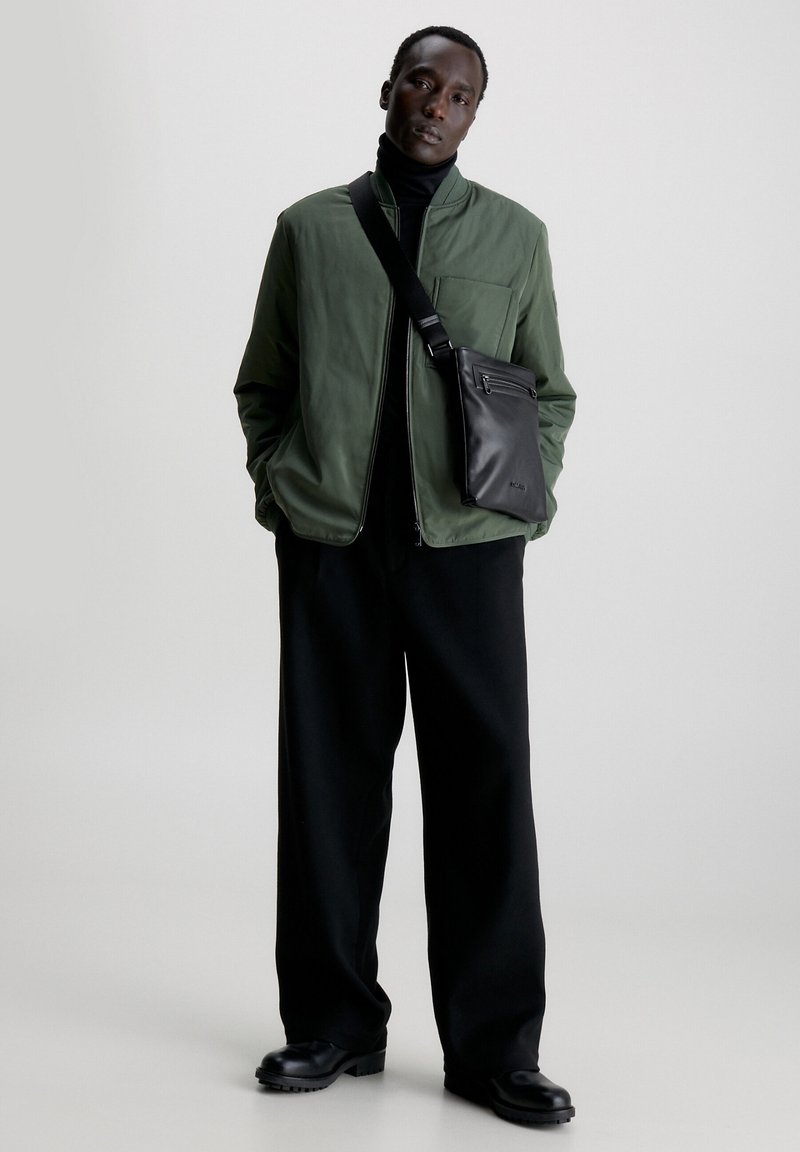 Giacca bomber verde, dolcevita nera, pantaloni larghi neri e borsa a tracolla nera. Texture lisce e elementi di design eleganti.