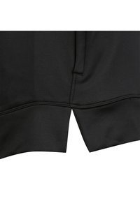 Zwarte hoodie zoomdetail, met een gestikte afwerking en een split aan de zijkanten voor een ontspannen pasvorm. De stof lijkt textuur te hebben en rekbaar te zijn.