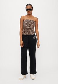 Top sem mangas com estampa de leopardo, calças de moletom pretas com logotipo, tênis brancos de plataforma, combinado com óculos de sol pretos. Tecido suave, corte casual.