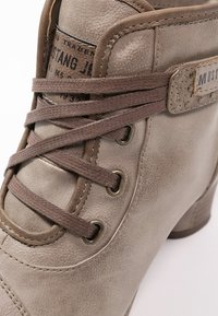 Šedé kožené kotníkové boty s hnědými tkaničkami, kovovými očky a štítkem "Mustang Jeans." Mají texturovaný povrch a nízký podpatek.