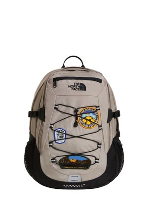 Lichtgrijze North Face rugzak met zwarte bodem, meerdere patches, elastische koorden en zij-netzakken.