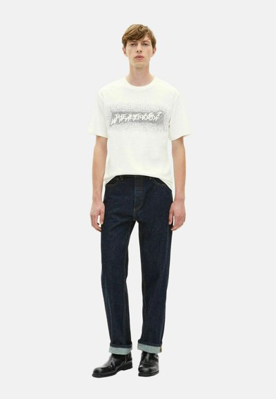 T-shirt de algodão branca com estampado gráfico em preto, combinada com jeans de ganga escura, com as mangas enroladas, e botas de couro pretas.