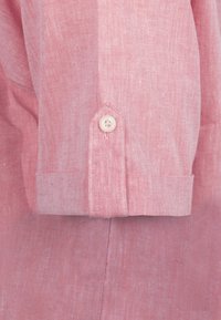 Camisa de lino rosa claro con puño abotonado y una textura sutil. Presenta un diseño de puño puntiagudo y un solo botón blanco.