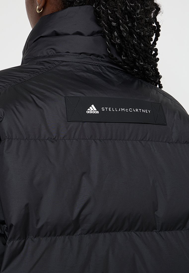 Czarna kurtka puchowa z wysokim kołnierzem, o teksturowanym, matowym wykończeniu. Posiada prostokątną czarną naszywkę z napisem "STELLAS McCARTNEY" oraz logo adidas.