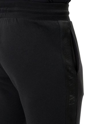 Pantaloni della tuta neri in tessuto morbido, con vita a coste, tasche laterali e motivo logo tonale lungo il fianco.