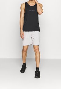 Czarny bawełniany top na ramiączkach z logo "CALVIN KLEIN", w połączeniu z jasnoszarymi szortami. Model nosi czarne buty sportowe, stojąc na jednolitym tle.