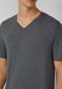 Szary t-shirt z dekoltem w serek, wykonany z lekkiej, teksturowanej tkaniny, z krótkimi rękawami i luźnym krojem, wyeksponowany na prostym tle.