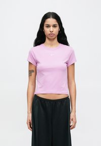 Λιλά βαμβακερό t-shirt με στρογγυλή λαιμόκοψη και κοντά μανίκια. Διαθέτει μικρό λευκό λογότυπο Nike στο στήθος. Συνδυάζεται με μαύρο παντελόνι.