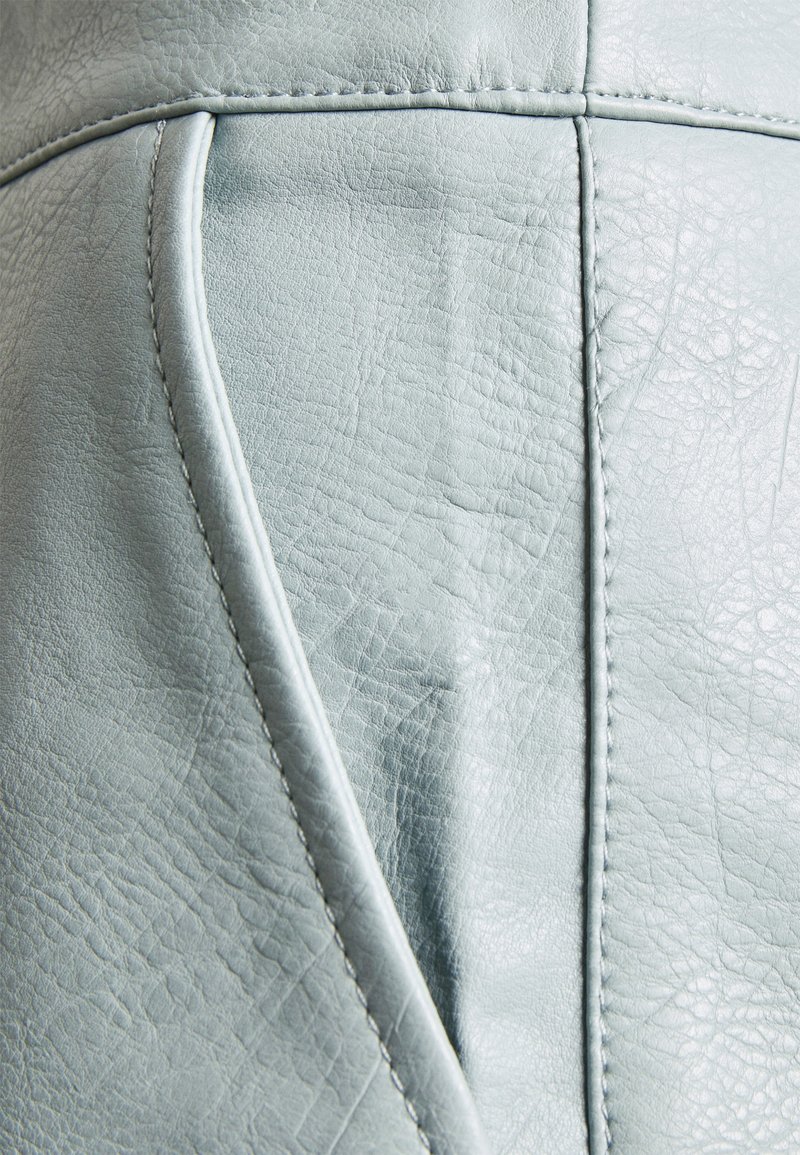 Gros plan d'un revêtement en cuir gris clair avec coutures visibles et détails de texture naturelle.