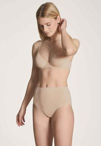 Bra beige in cotone misto con coppe morbide e spalline regolabili abbinato a slip beige a vita alta. Texture liscia e design senza cuciture.