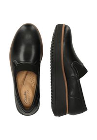 Mocassins en cuir noir avec une semelle en caoutchouc marron clair, présentant une finition lisse et des empiècements élastiques sur les côtés pour faciliter l'enfilage.