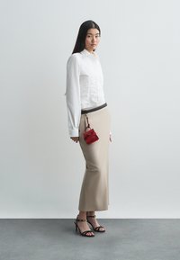 Camicia bianca con bottoni e dettagli arricciati, gonna a matita beige, sandali neri con tacco alto e una piccola borsa rossa attaccata a una cintura nera.