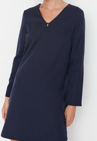 Robe longue à manches longues bleu marine avec un décolleté en V et un petit détail découpé à l'avant. Texture lisse, coupe décontractée, longueur au-dessus du genou.