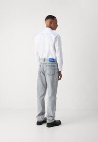 Hvit skjorte med lange ermer og krage, kombinert med lysegrå denimjeans med et blått merke på baksiden. Svarte sko fullfører antrekket.