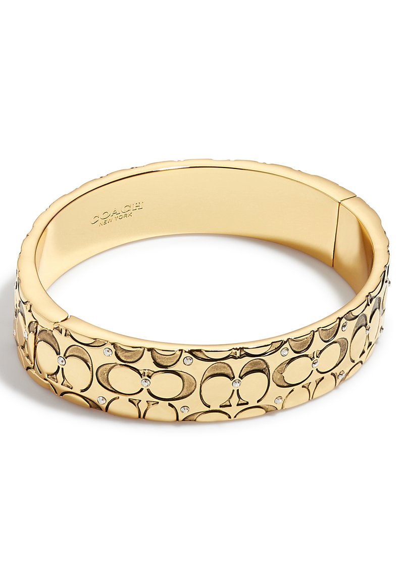 Armbandet i guldton har präglade cirkulära mönster och små klara stenar. Den släta metallytan har en polerad yta.