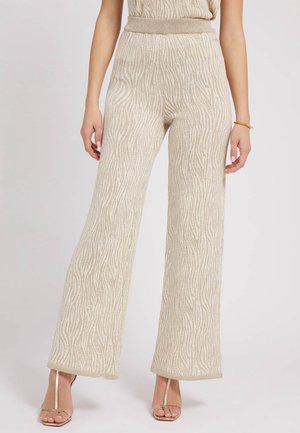 Beige bukser med vidt ben og høj talje med subtil zebra-print, båret med guldfarvede remsandaler og en matchende top.