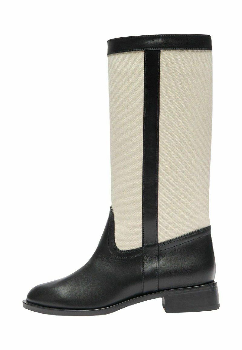 Bota hasta la rodilla con pie y ribete de cuero negro, eje de tela beige, tacón bajo y puntera redondeada, mostrada de lado sobre un fondo blanco.