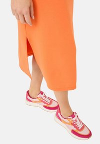 Orange midi-klänning med sidoklyv, i kombination med rosa och vita sneakers med mesh- och mockadetaljer, som visar olika nyanser av rosa.