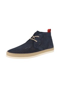 Scarpe alla caviglia in suede perforato di colore blu navy con suola in gomma beige e lacci beige. Il tab del tallone rosso aggiunge un tocco di contrasto.