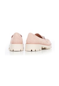 Un par de mocasines de ante color rosa empolvado con suelas gruesas de goma blanca, mostrados desde la parte trasera sobre una superficie reflectante blanca.