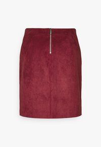 Bordová semišová sukně s přiléhavým střihem, která má přední zip a hladkou texturu. Krátká délka s minimálními detaily.