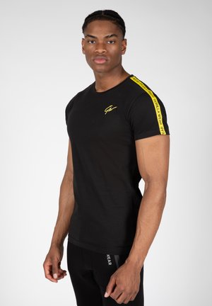 Zwarte t-shirt met korte mouwen en een slim-fit ontwerp. Bevat een geel logo en contrasterende gele tape langs de schouder. Gemaakt van een katoenmix.